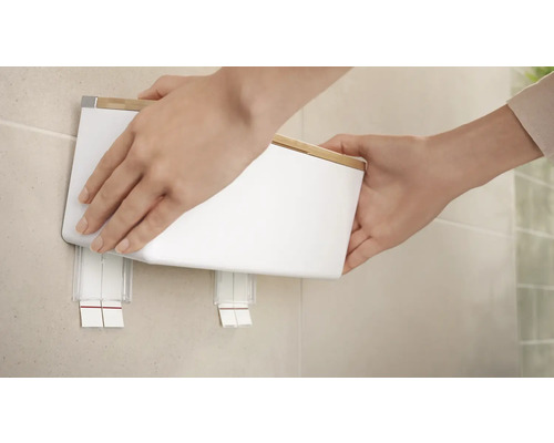 Persoon bevestigt een witte wandcosmeticabak met bamboedeksel aan een muur