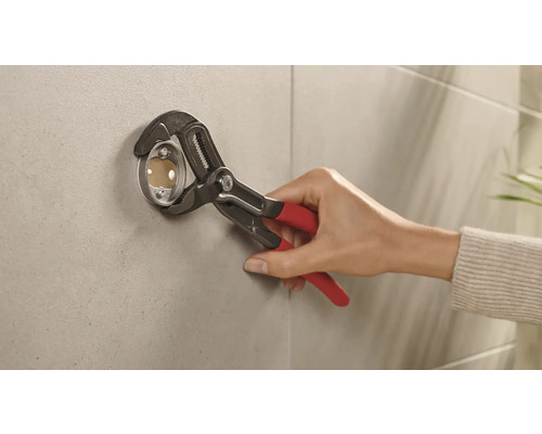 Installateur bevestigt een rozet met een waterpomptang aan een wand.