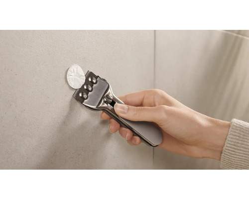 Een persoon gebruikt een schraper om lijmresten van tegels te verwijderen.