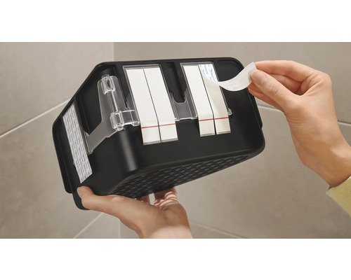 Persoon verwijdert beschermfolie van kleefstrips op een zwarte plank voor badkameraccessoires.