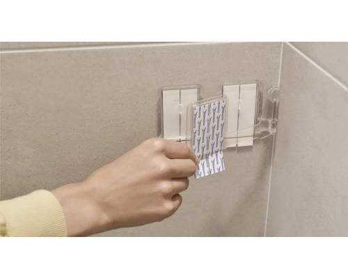 Persoon bevestigt plakstrips aan een houder in de badkamer.