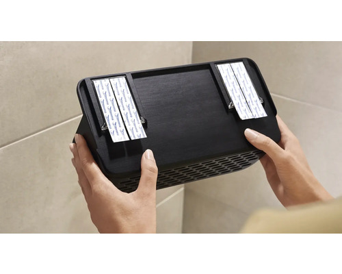 Persoon bevestigt zwarte wandventilator met plakstrips aan de muur