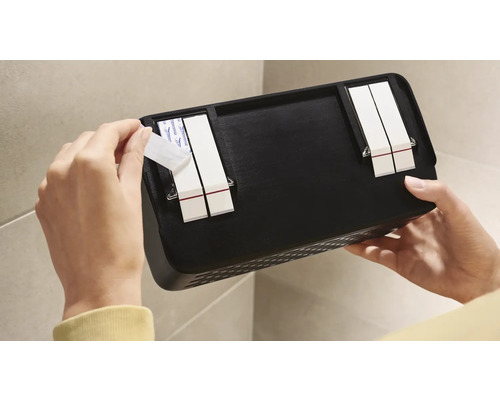 Persoon bevestigt een zwarte wandplank met plakstrips aan een muur