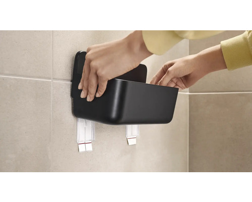 Persoon bevestigt een zwarte opbergdoos met zelfklevende bevestiging aan de muur