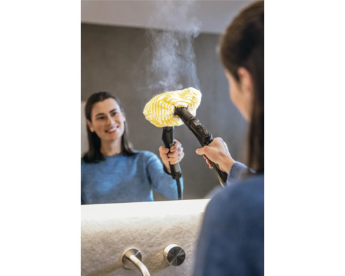 Vrouw gebruikt een stoomreiniger met gele doekbevestiging op een spiegel in de badkamer