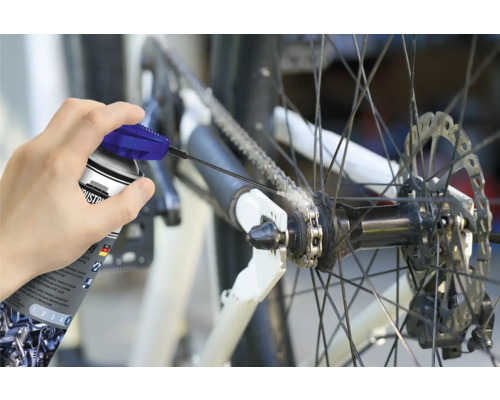 Een persoon smeert de ketting van een fiets met een kettingspray.