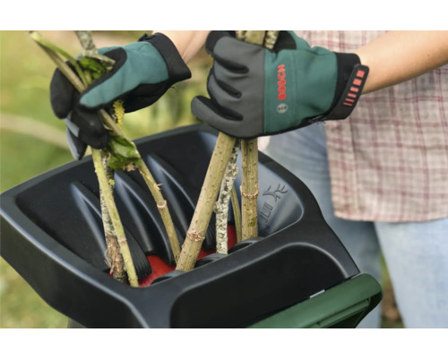 Twee handen met tuinhandschoenen vullen een hakselaar met takken.