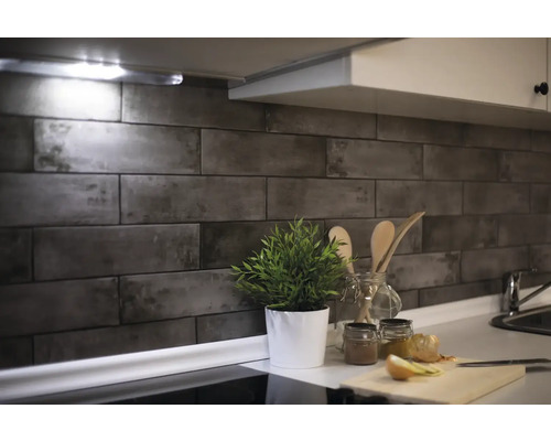 Keukenscène met wandtegels in steenlook, plant en keukengerei op het aanrecht.