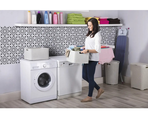 Lichte wasruimte met wasmachine, wasdroger, wasmand, waskist, plank en een vrouw die een wasmand draagt.