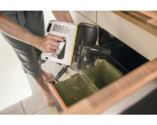 Een persoon leegt een draadloze stofzuiger boven een vuilnisbak.