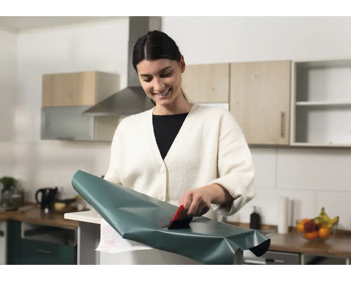Vrouw brengt decoratieve folie aan met een rakel in de keuken