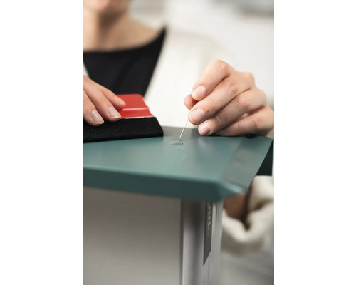 Persoon verwijdert luchtbellen uit een folie met een naald en een rakel.