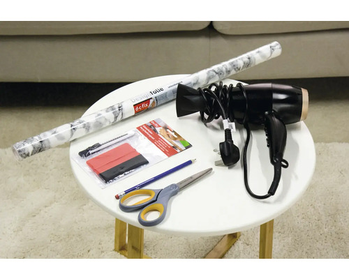 Decoratiefolie, rakel, cutter, föhn, potlood en schaar op een tafel