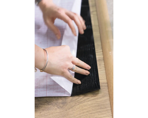 Een persoon verwijdert de beschermfolie van een zelfklevende vloertegel.