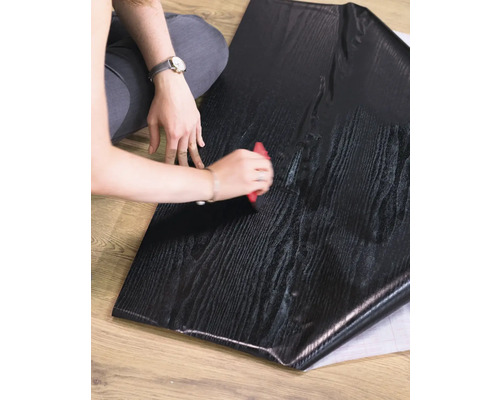 Persoon verwerkt zelfklevende meubelfolie met houtlook met een rakel.