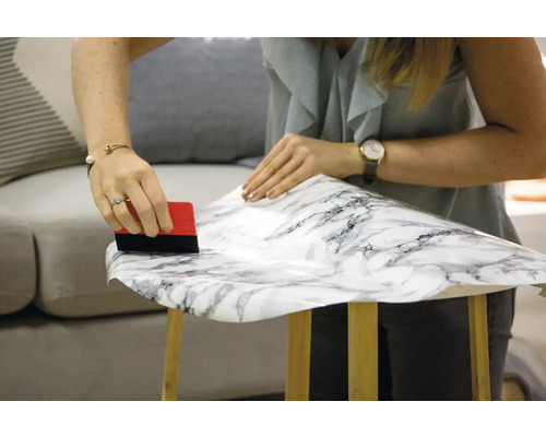 Vrouw brengt decoratieve folie met marmerpatroon aan op tafel