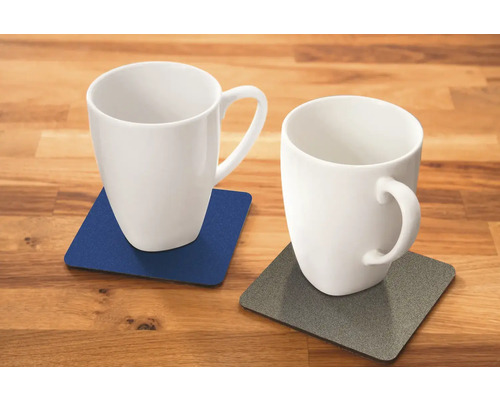 Twee witte mokken op onderzetters op een houten tafel.