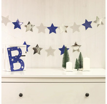 Decoratieve scène met sterrenslinger, decoratieve letter, kerstbomen en kaarsen op een ladekast