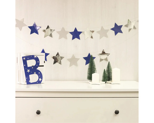 Decoratieve scène met sterrenslinger, decoratieve letter, kerstbomen en kaarsen op een ladekast