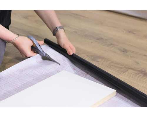 Persoon snijdt met een schaar een folie op maat om een meubelstuk te beplakken