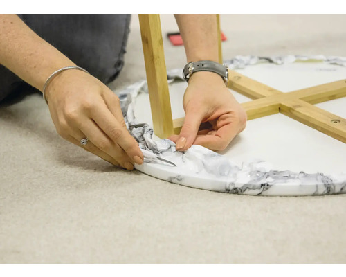 Close-up van een persoon die verpakkingsmateriaal verwijdert van een ronde tafel met houten poten.