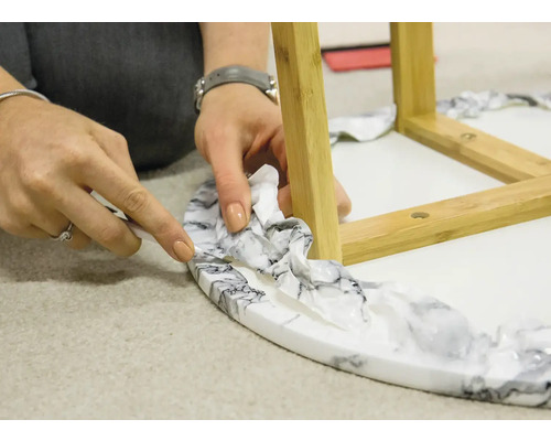 Een persoon snijdt met een mes folie van een ronde tafel met bamboepoten