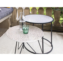 Twee ronde bijzettafels met tafelbladen in steenlook, een waterfles en een drinkglas staan op een balkon.