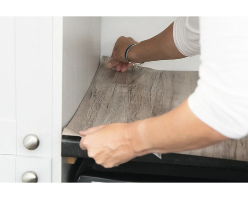 Iemand brengt meubelfolie met houtlook aan in een keuken.