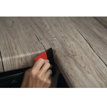 Iemand brengt een houten decoratiefolie aan met een rakel