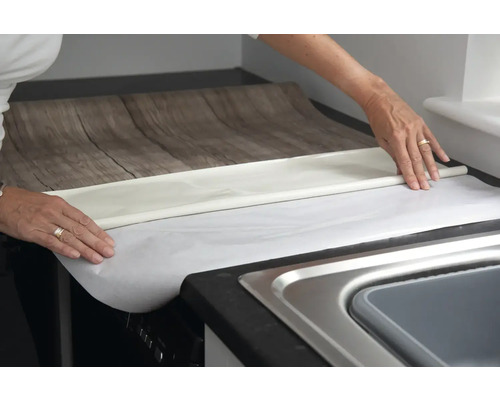 Een persoon brengt meubelfolie met houtlook aan op een aanrecht.