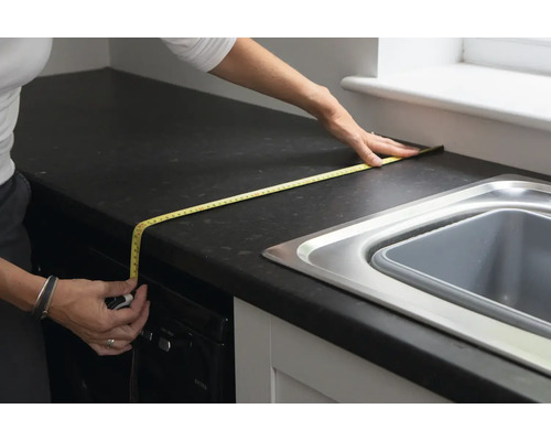 Een persoon meet een aanrecht met een meetlint.