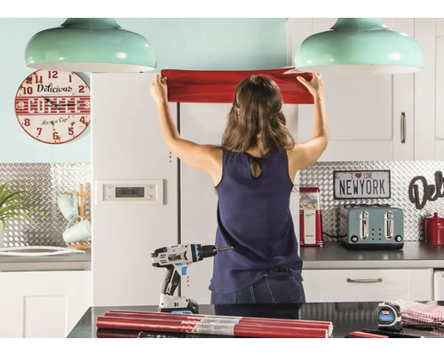 Vrouw bevestigt meubelfolie in een keuken met gereedschap en decoraties.
