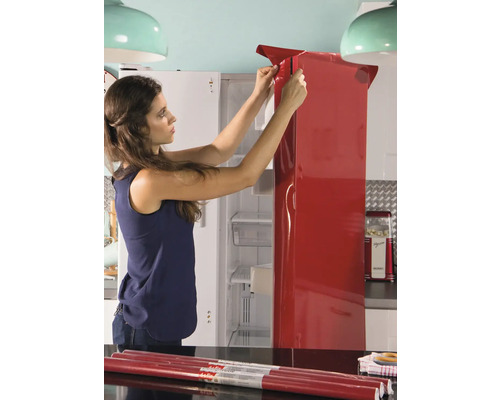 Vrouw brengt een rode meubelfolie aan op een koelkast.