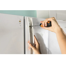 Een persoon bevestigt met een schroevendraaier een beugel aan een wit oppervlak.