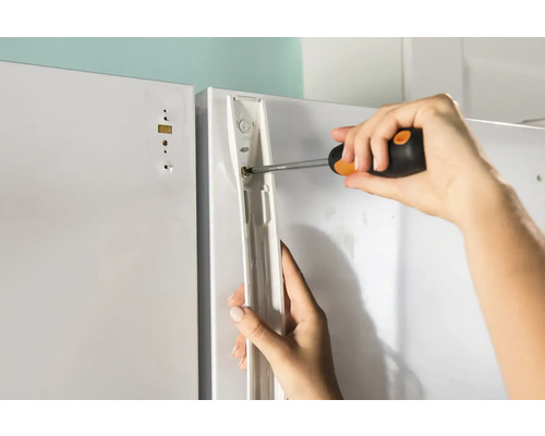 Een persoon bevestigt met een schroevendraaier een beugel aan een wit oppervlak.