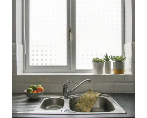 Keukenscène met raamfolie met vierkant motief, gootsteen en decoraties.