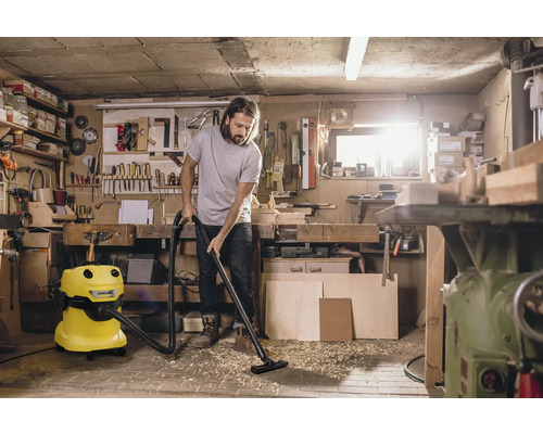 Man zuigt een werkplaats met een gele Kärcher alleszuiger.