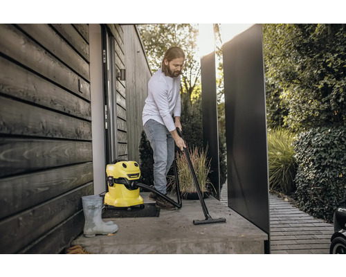 Een man maakt met een gele alleszuiger een terras voor een huis schoon.