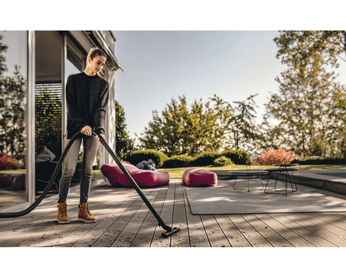 Een vrouw maakt een houten terras schoon met een stofzuiger voor buiten.