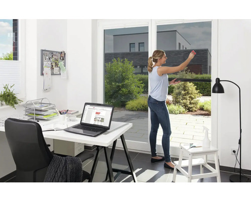 Vrouw brengt zonwerende folie aan op raam, kantoor op de achtergrond