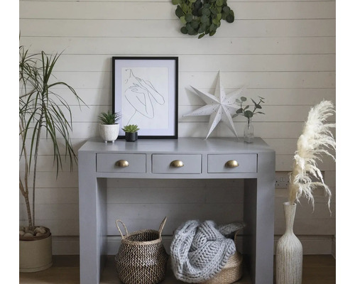 Decoratief interieur met console, kunst, planten en manden in een heldere ruimte.