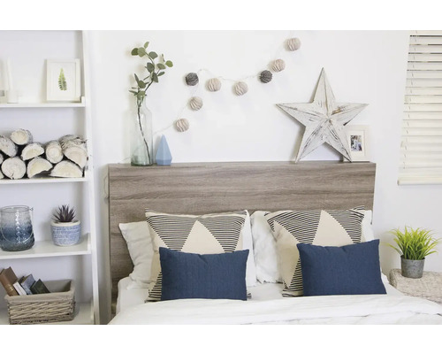 Slaapkamer met bed, houten hoofdeinde, kussens en decoratieve elementen zoals een lichtketting en een houten ster