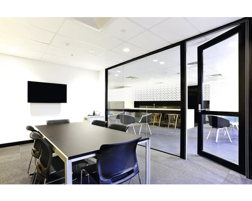 Lichte vergaderruimte met glazen wand, tafel, stoelen en scherm.