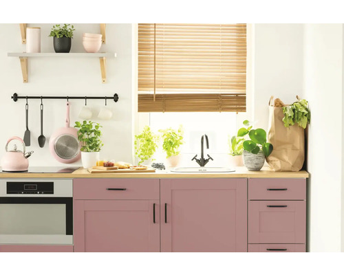 Lichte keuken met roze kasten, houten jaloezieën en diverse keukengerei.