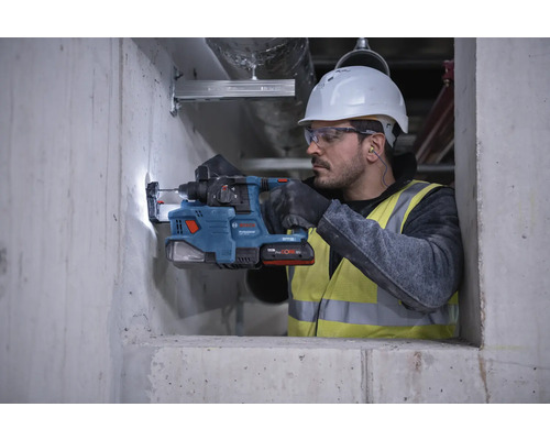 Een arbeider boort met een boorhamer een gat in een betonnen muur.