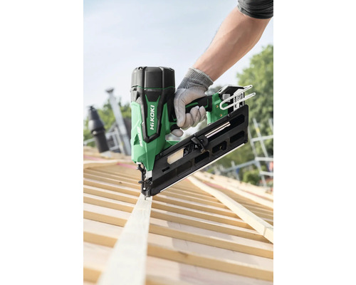 Een persoon bevestigt een houten plank op een dakspant met een groene HiKoki accu-spijkermachine.