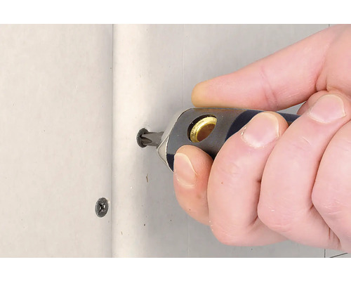 Een persoon schroeft een schroef met een schroevendraaier in een muur.