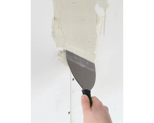 Een hand strijkt gips glad op een muur met een plamuurmes.