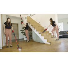 Vrouw gebruikt draadloze stofzuiger in huis op de vloer, het plafond en de trap