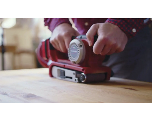 Een persoon gebruikt een bandschuurmachine op een houten oppervlak.